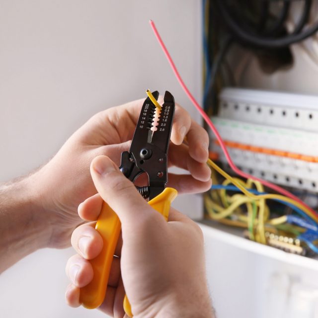 Young electrician skinning a wire in light room